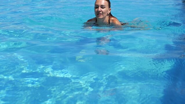 Slow motion footage of a woman sitting in a pool, enjoying the sun, and swimming in the pool.