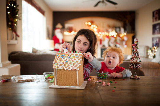 Two kids decorating a gingerbread house for the holidays at home