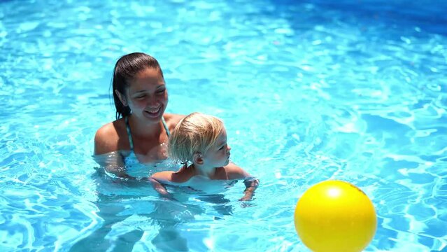 Mom supports a little girl swimming in the pool to the ball. High quality 4k footage