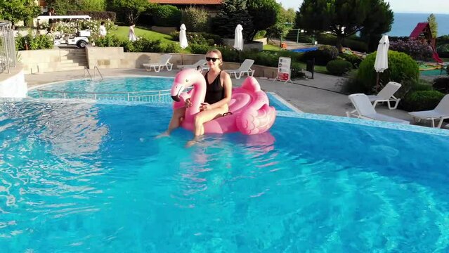 Aerial drone view of woman on pink flamingo pool float in pool in hotel. Summer holidays, enjoying summer vacations footage from above
