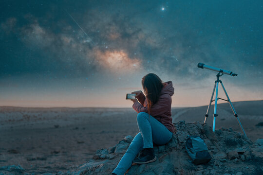 Lonely traveler woman sitting in a remote desert place taking photos with her cell phone of the night sky