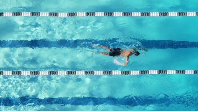 An impressive aerial 4K footage shows a swimmer in a pool during sunrise, elegantly swimming in slow motion, emphasizing their serene strokes