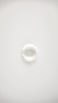 Fresh milk drop falling and splashing in a milky pool from above. Slow motion rings and ripple top view. Vertical footage