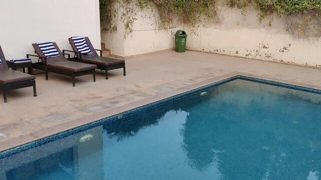 Footage of a swimming pool, trees , chairs in a hotel shot during daylight. Blue reflecting pool urban city architecture scenic environment
