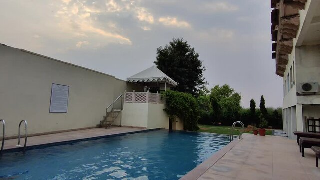 Time lapse footage of a swimming pool, trees , chairs in a hotel shot during daylight. Blue reflecting pool urban city architecture scenic environment
