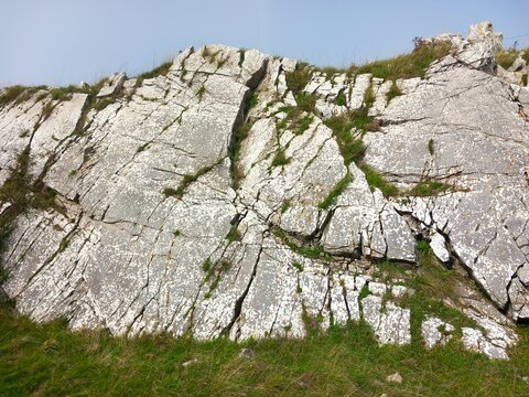 Rocky cliff with grass and blue sky in background, closeup of photo