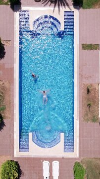 Man dives to swimming pool and woman going out of swimming pool. Real time top down aerial video footage of man jumping to the turquoise colored water of swimming pool. Summer leisure activities