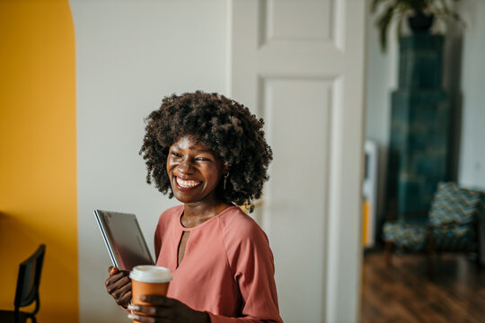 A modern black woman with a coffee cup smiles confidently in an office environment, embodying positivity and style