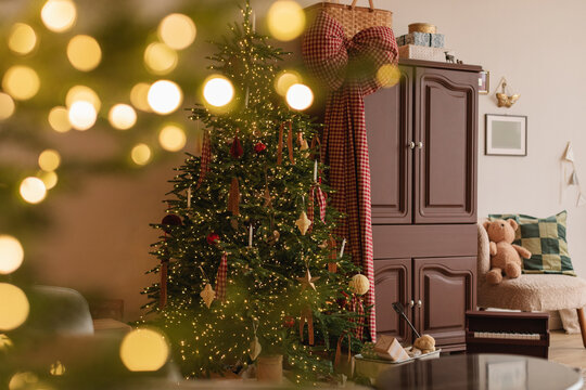 Illuminated Christmas tree next to a cupboard and wagon with wrapped Christmas gifts in a living room