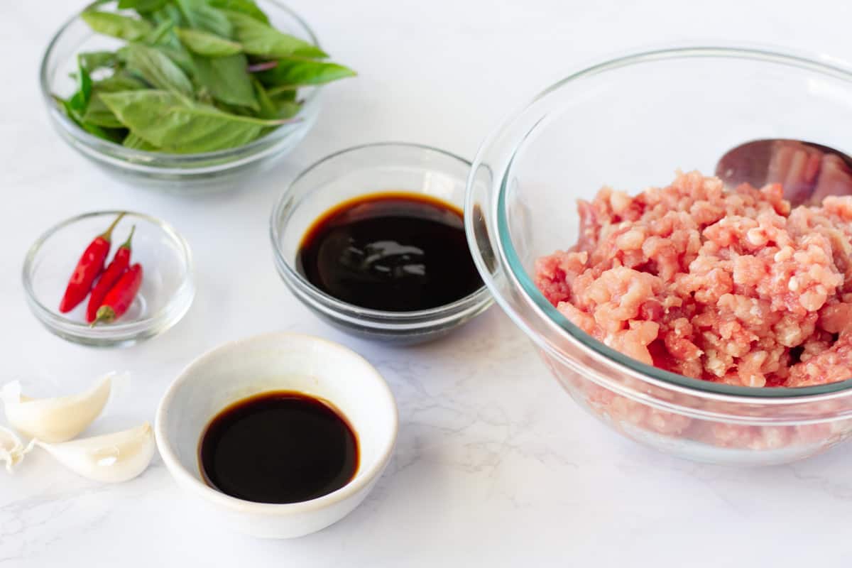 Ingredients in bowls, ground pork, soy sauce, oyster sauce, basil, garlic, and chilis.