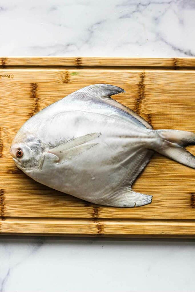 raw whole pomfret on the cutting board before cooking