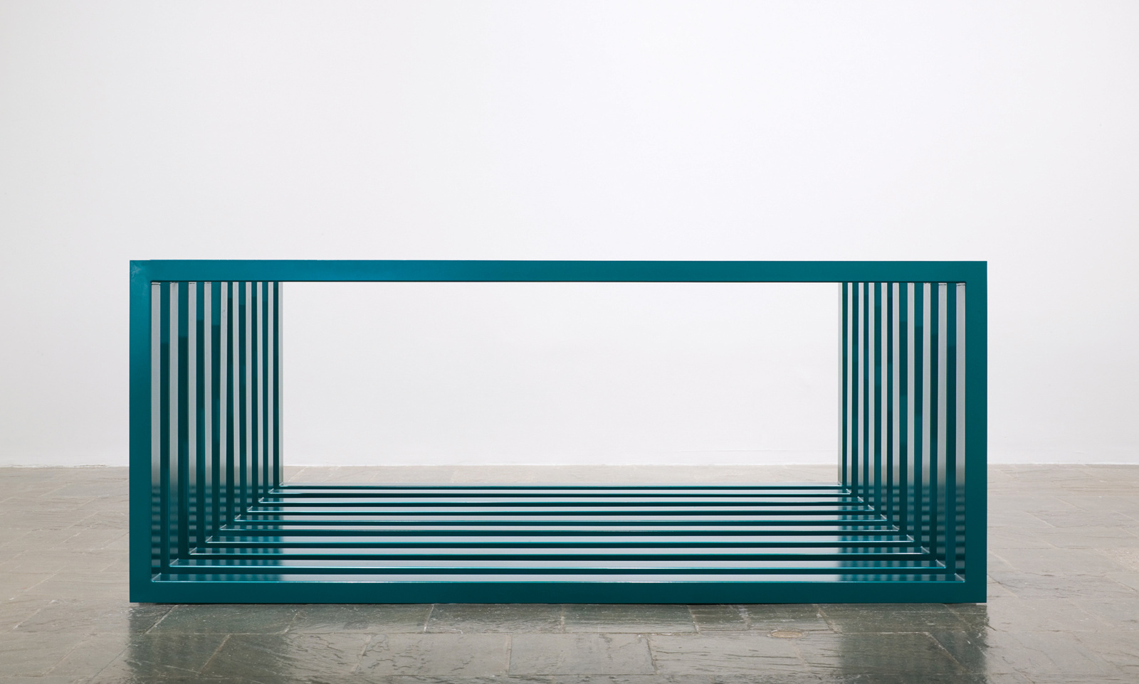 A minimalist teal-colored metal bench with vertical slats creating an optical illusion, placed on a grey floor against a white wall.