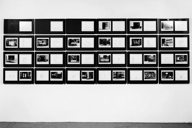 A gallery wall with a series of framed black and white photographs and text panels in a symmetrical arrangement.