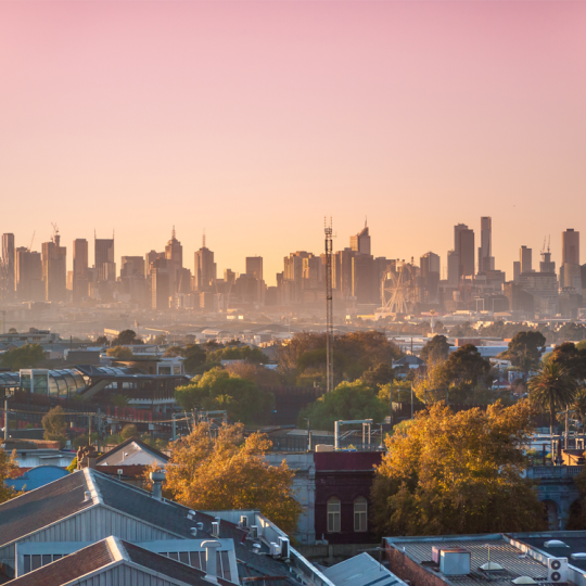 The Melbourne city skyline at dusk. There are inner-suburban houses and buildings in the foreground.