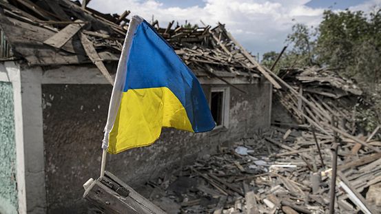 Drapeau ukrainien flottant au vent devant une maison détruite par la guerre