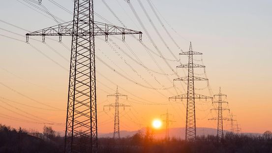 La photo montre des pylônes électriques au coucher du soleil.