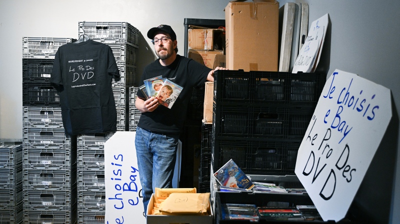 Jean-François Hall poses next to crates of DVDs in his home in Montreal, December 12, 2024. Hall buys and sells DVD's on eBay and facebook. (THE CANADIAN PRESS/Graham Hughes.)