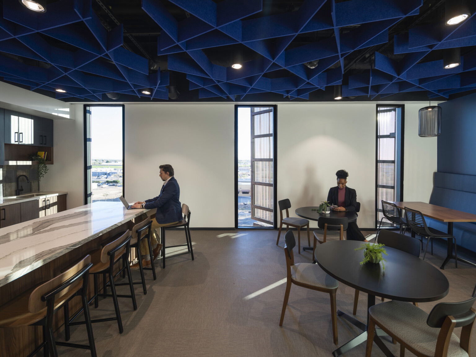 Office common space with blue accent wall and textural ceiling over mixed seating and marble counter, kitchenette left