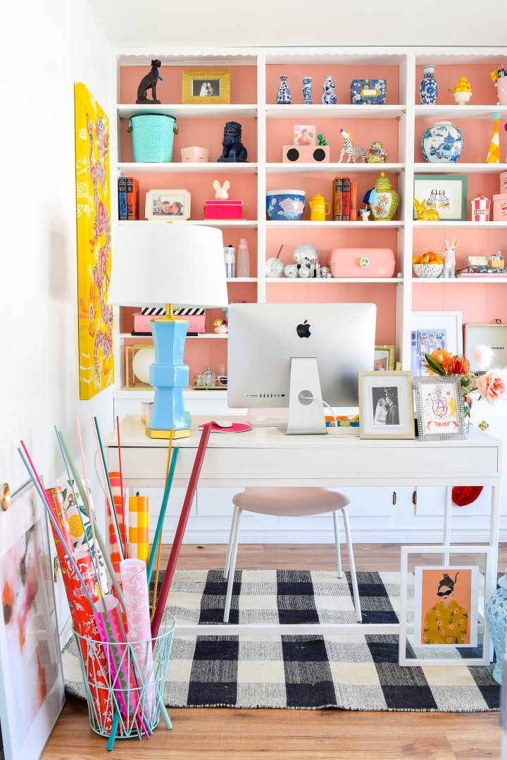 White home office desk in front of bookshelves that are painted pink