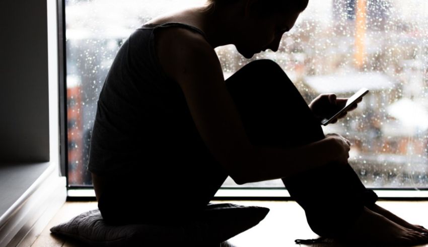 A woman sitting in front of a window looking at her phone.