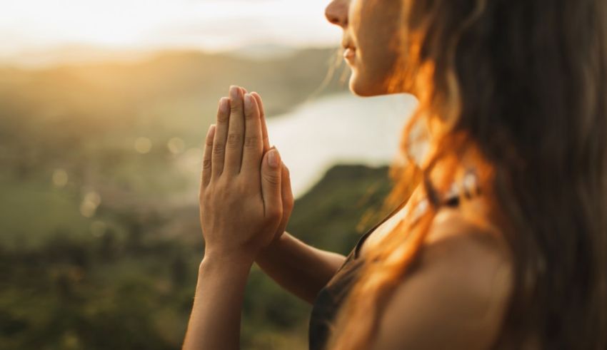 A woman is praying in front of a mountain at sunset.