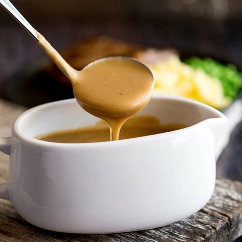 close up on a ladle of gravy pouring into a white gravy boat