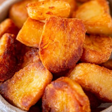 A close-up view of roasted potato chunks, piled in a bowl, showcasing their crisp, flaky edges.