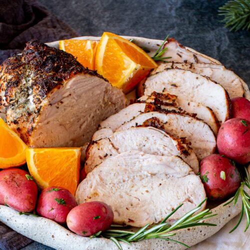 A dinner platter featuring sliced turkey breast, orange wedges, red potatoes, and rosemary, captured from a slightly angled view.