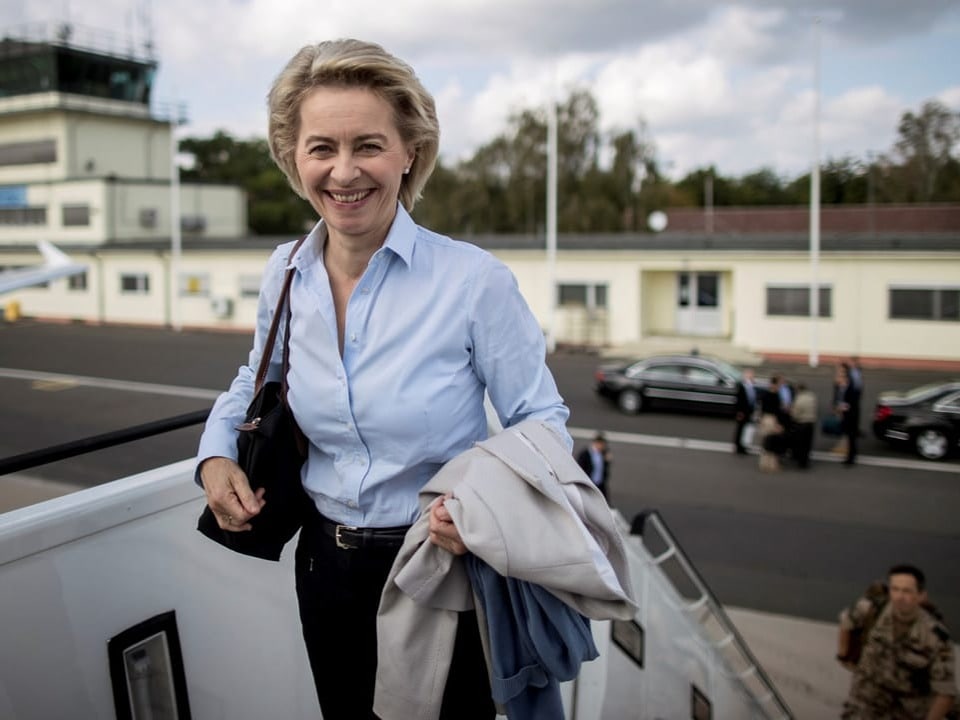 Frau steigt Treppe hinauf zu Flugzeug, Flughafen im Hintergrund.