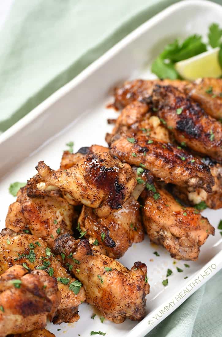 Chili Lime Chicken Wings piled on a white, rectangle platter with cilantro and lime wedges in the corner, sitting on a pale green napkin